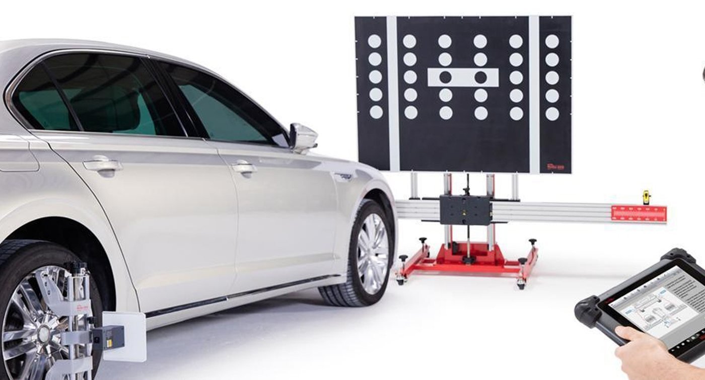 A car in front of an ADAS calibration target board, with the technician's tablet in shot